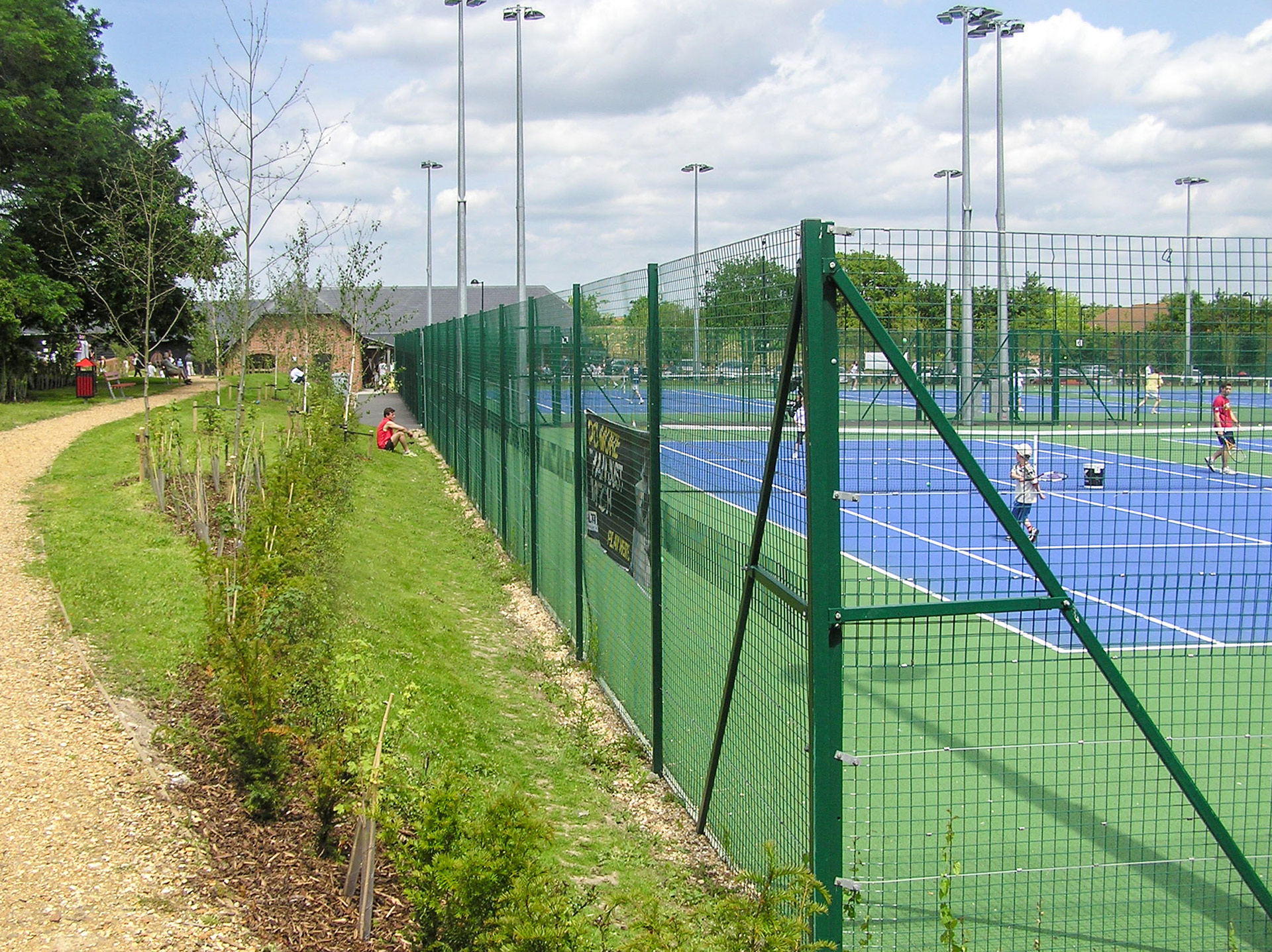 side view of fenced tennis courts from path