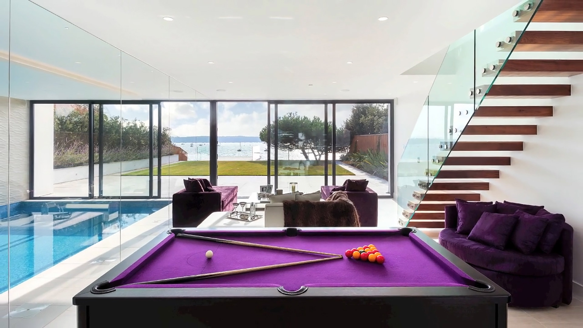 interior games room and indoor swimming pool with glass doors leading out to the garden with beautiful sea views