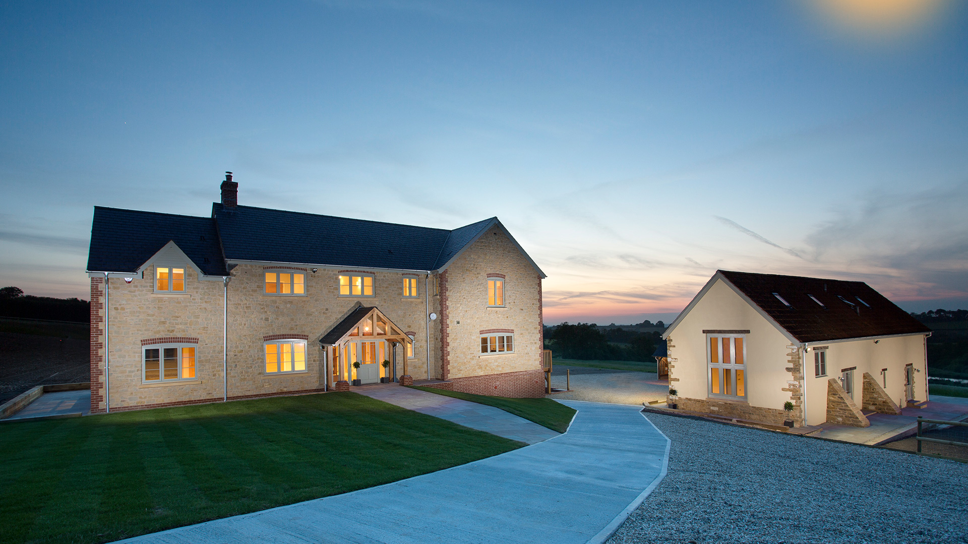 New large farmhouse and outbuilding with lights of at dusk