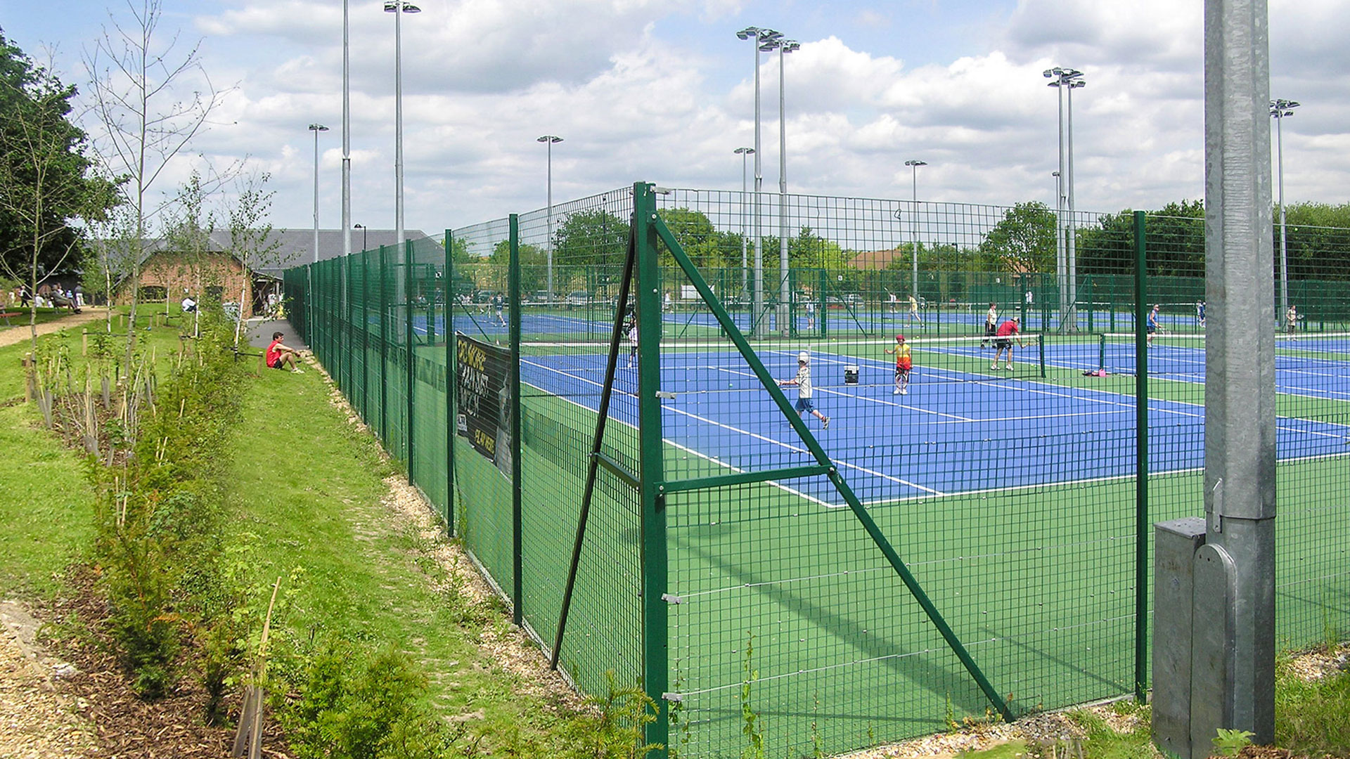 side view of fenced tennis courts from path
