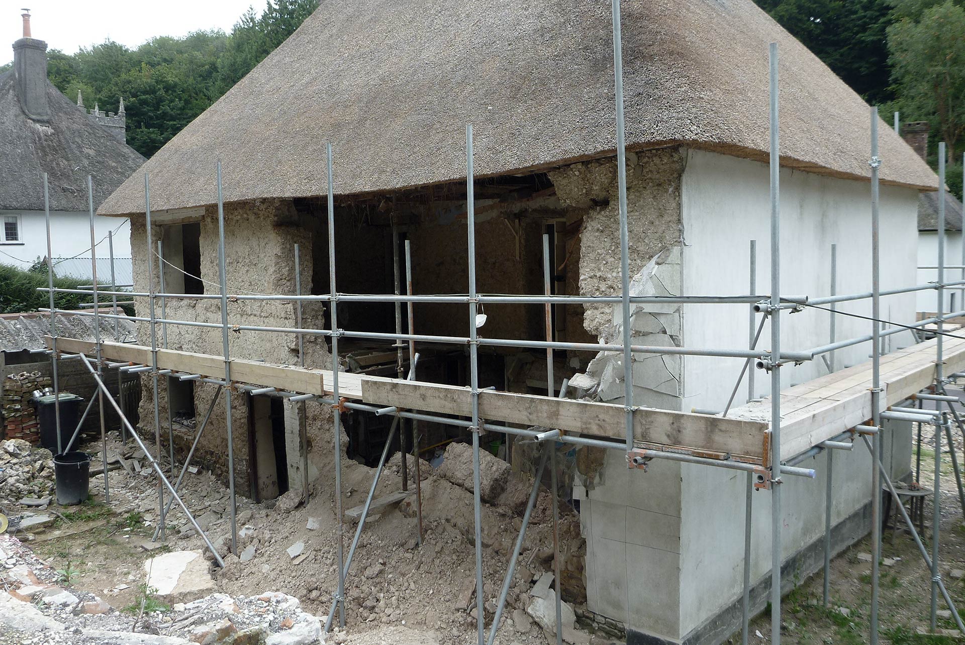 collapsed wall on house with scaffolding around and thatched roof