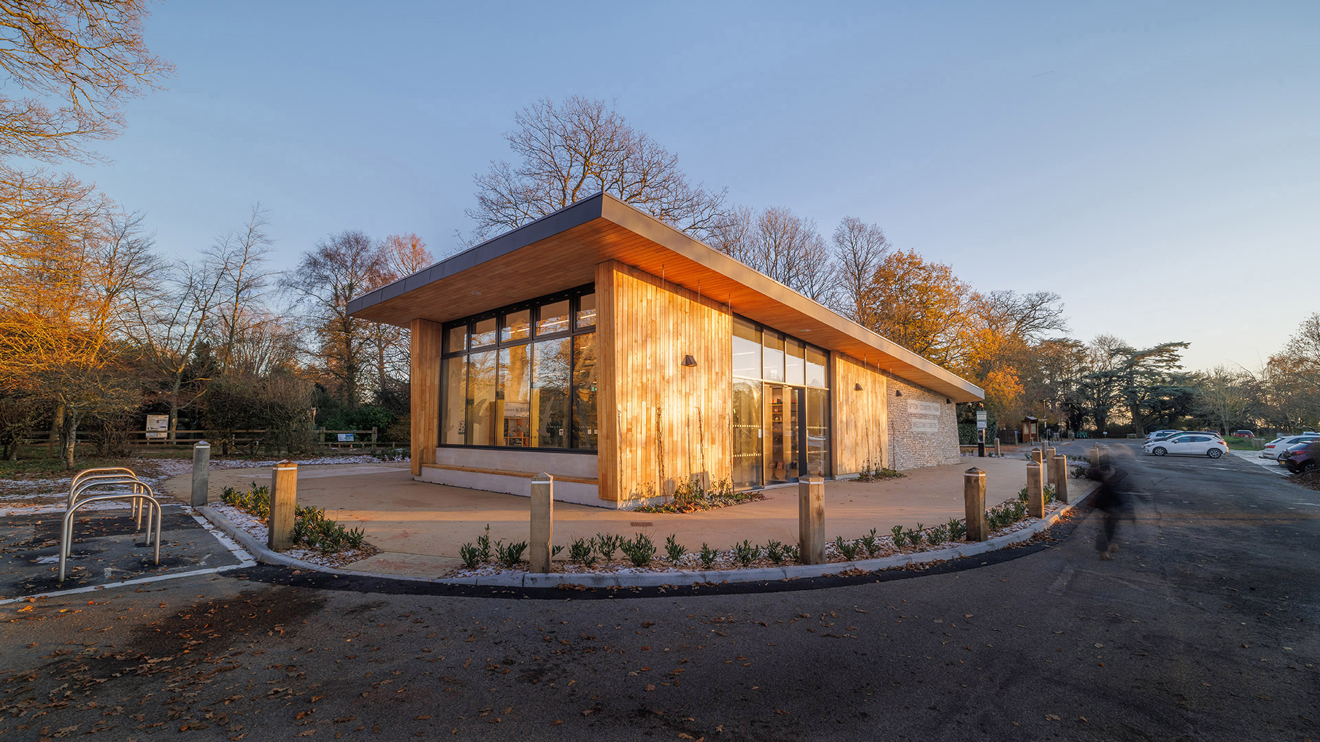 information centre with wood cladding and sloping roof at dusk with car park behind
