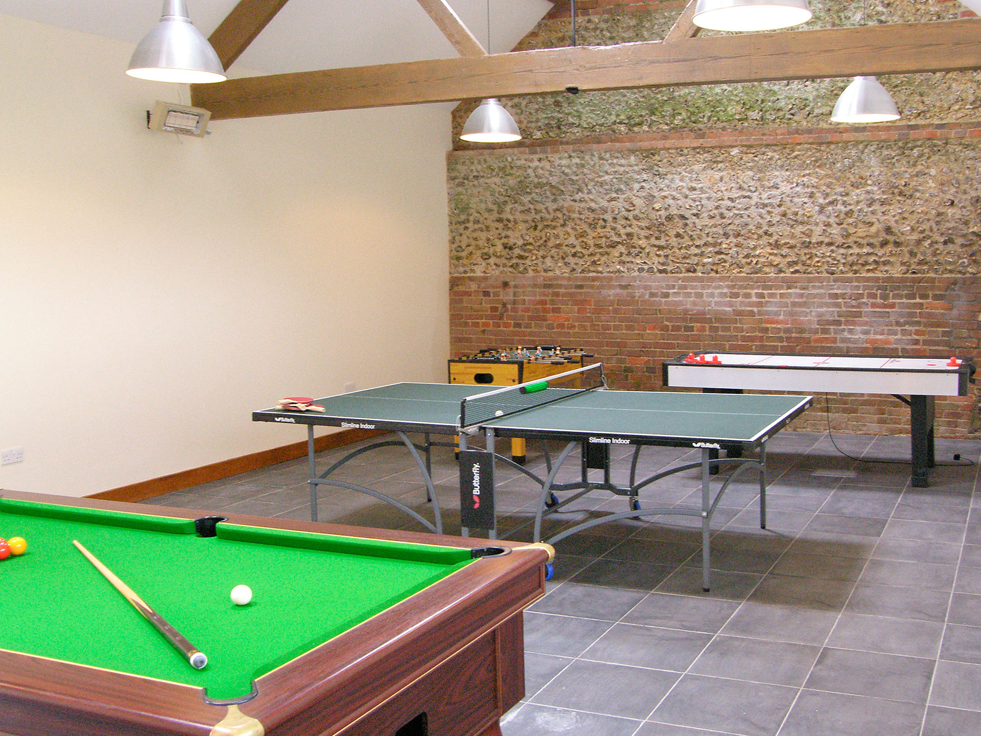 Interior games room of barn conversion with feature brick and stone wall and exposed beams