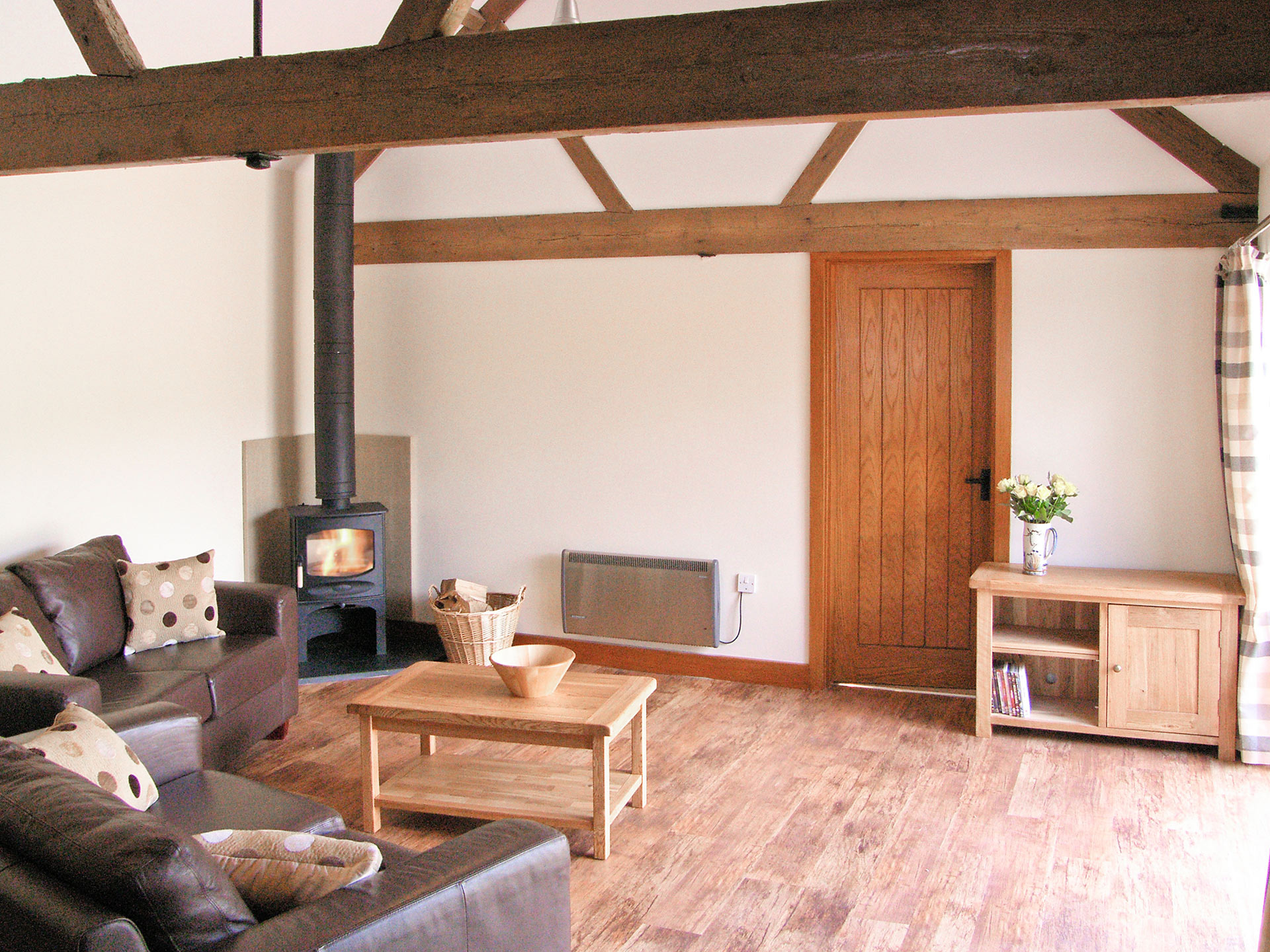 living space in neutral tones with wood burner and exposed wooden beams