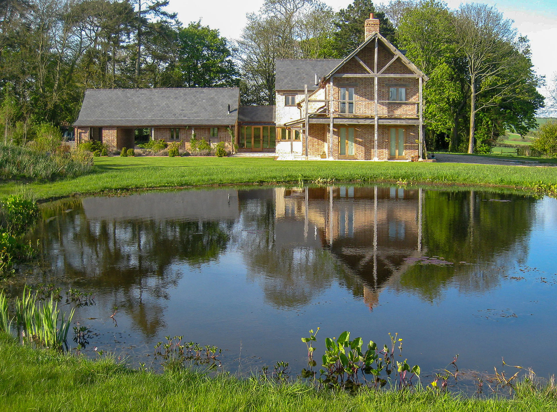 beautiful red brick and stone house with gable end overlooking a large pond and grass lawn