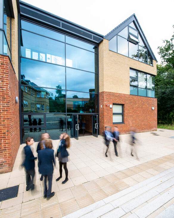 external entrance view of red brick school with large glass windows and glass corners