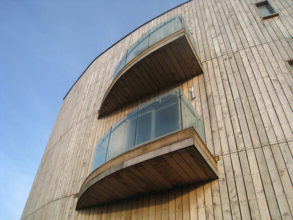 detail view of wooden clad building looking up with two glass balconies