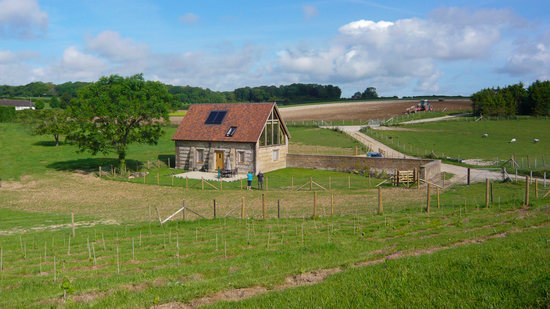 distant view of converted barn with red roof and solar panel surrounded by fields