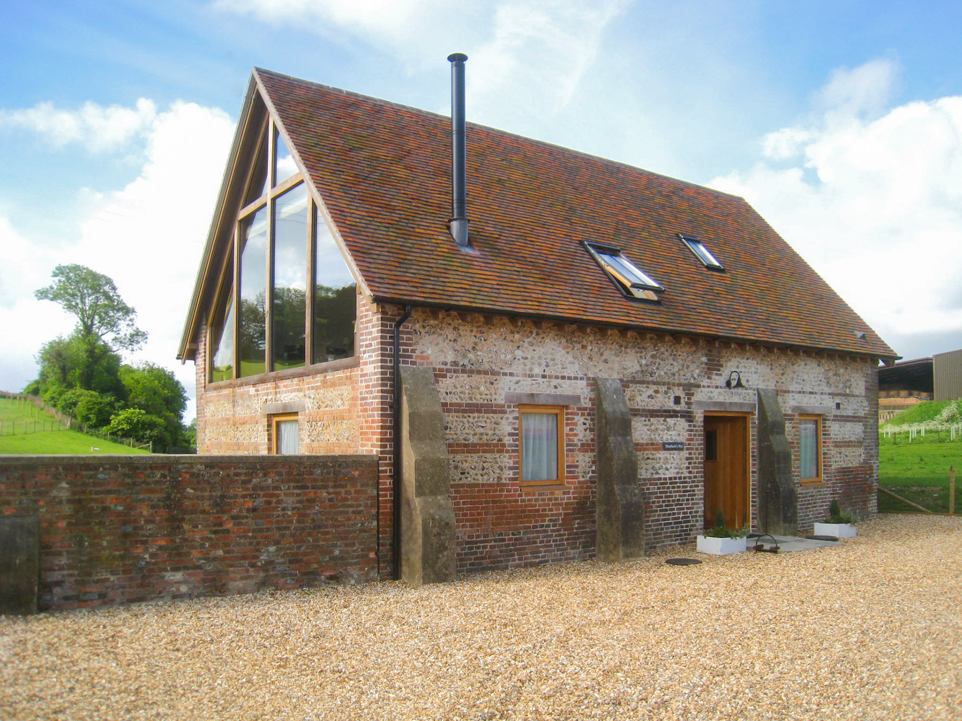 view from front drive to converted red brick shepherds hut with tall chimney and roof lights