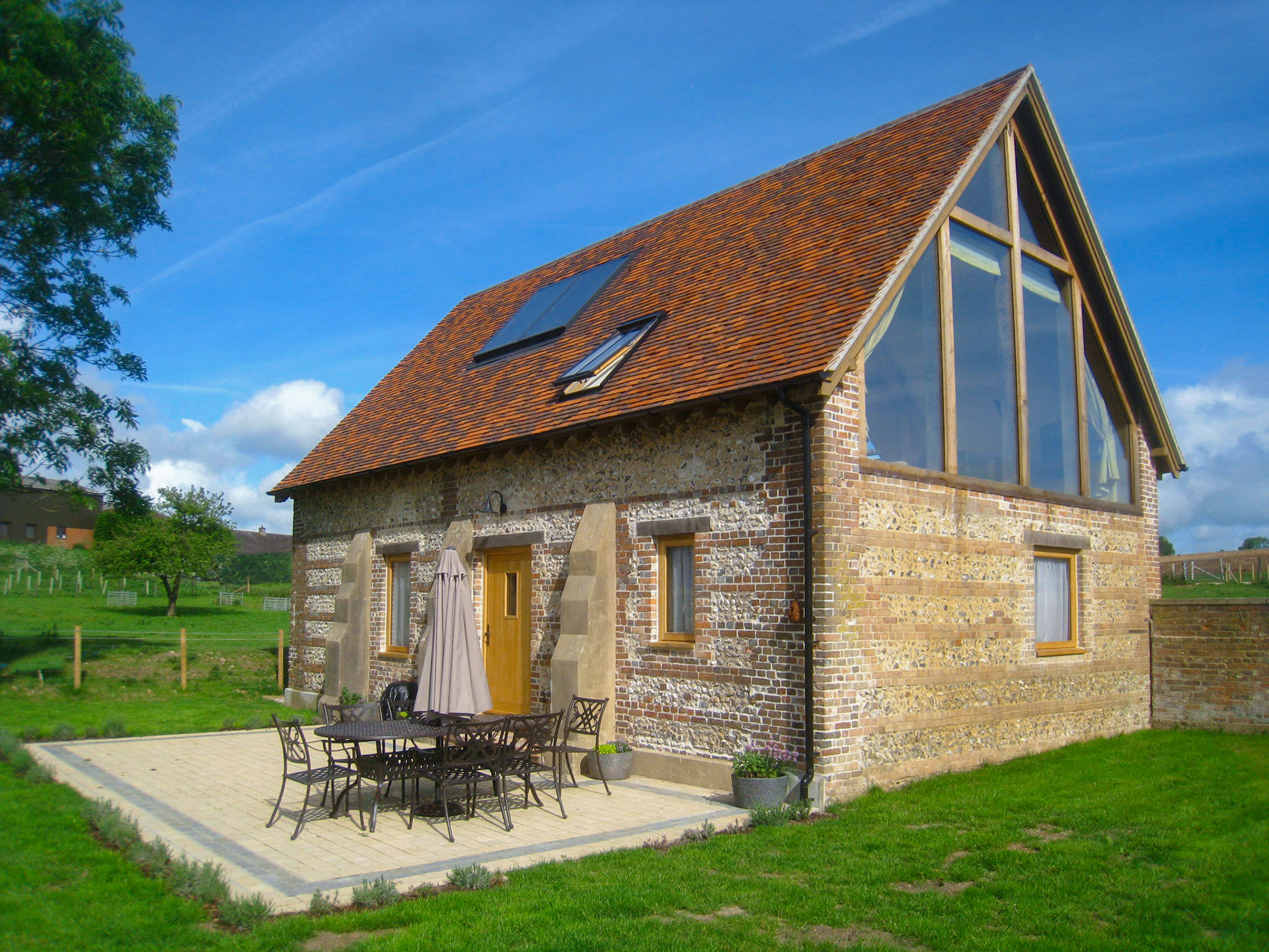 view from rear garden of brick shepherds hut with red tiled roof and roof lights