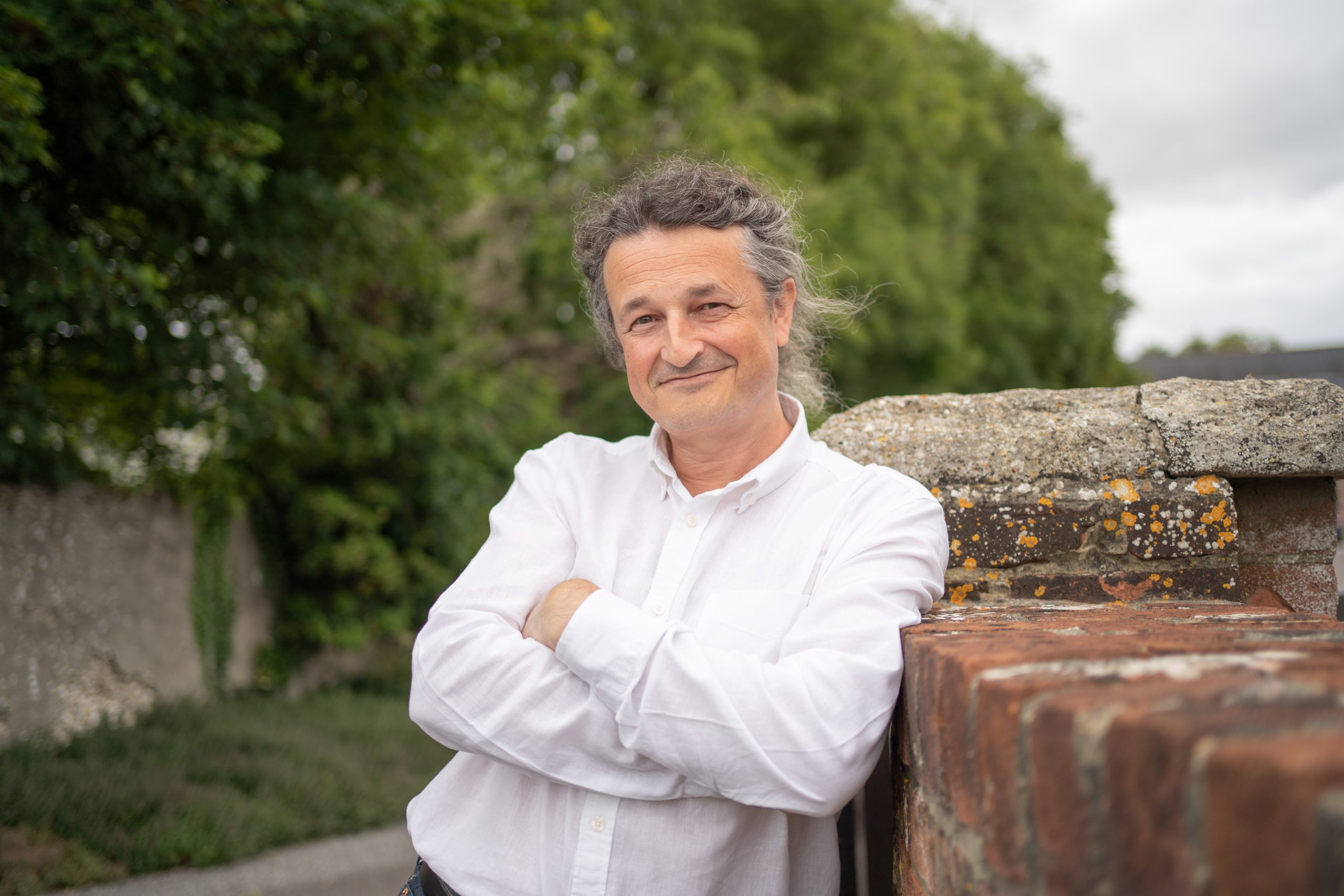 man smiling at camera with arms crossed leaning against a brick wall