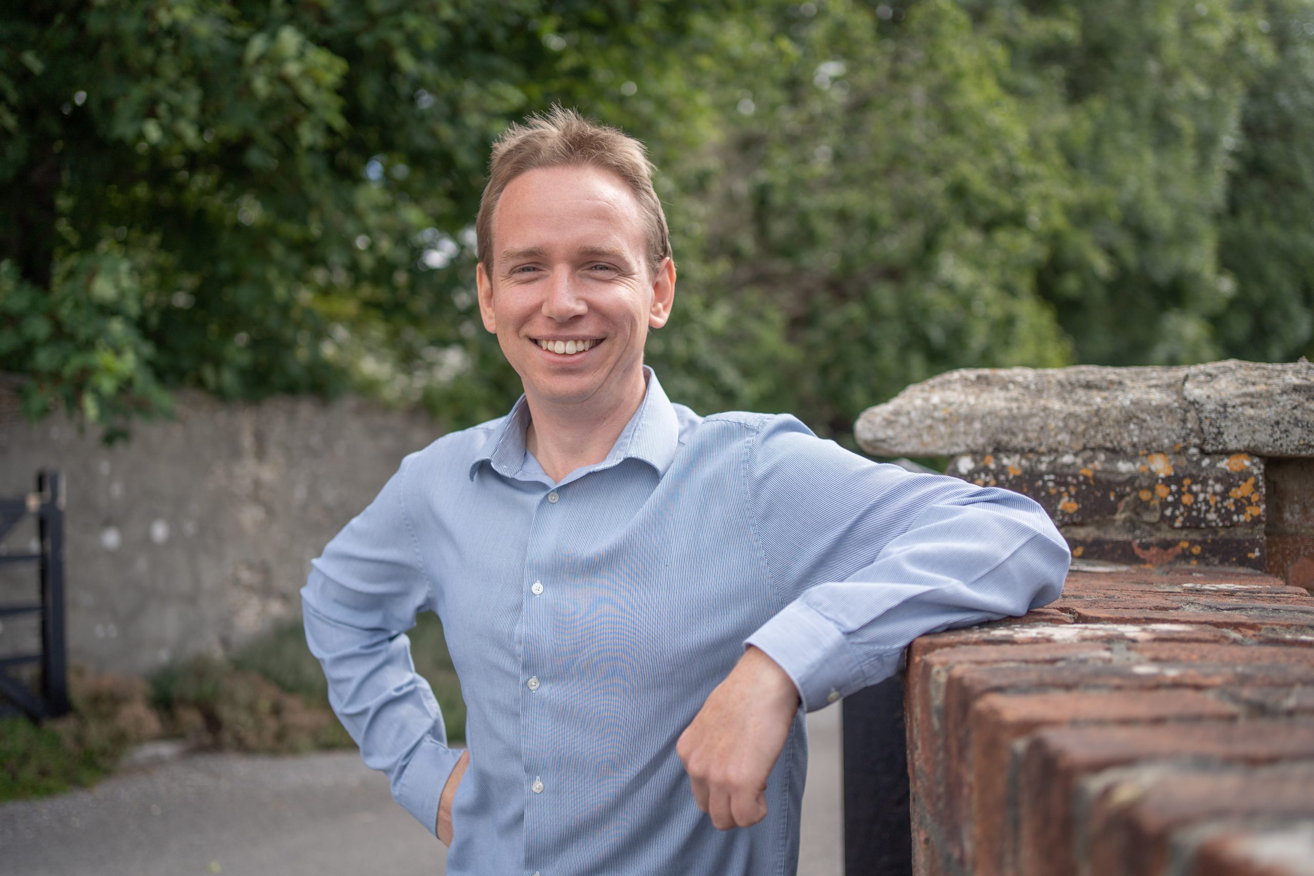 man smiling looking at the camera with arm leaning on brick wall