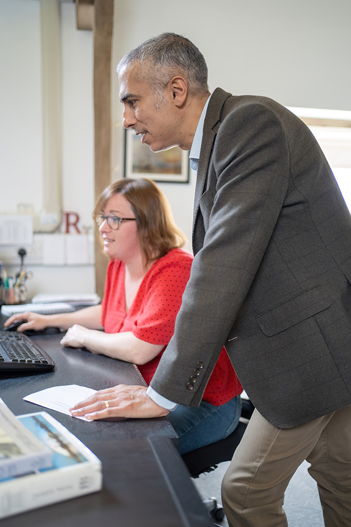 woman sat down and men standing leaning on desk looking at computer