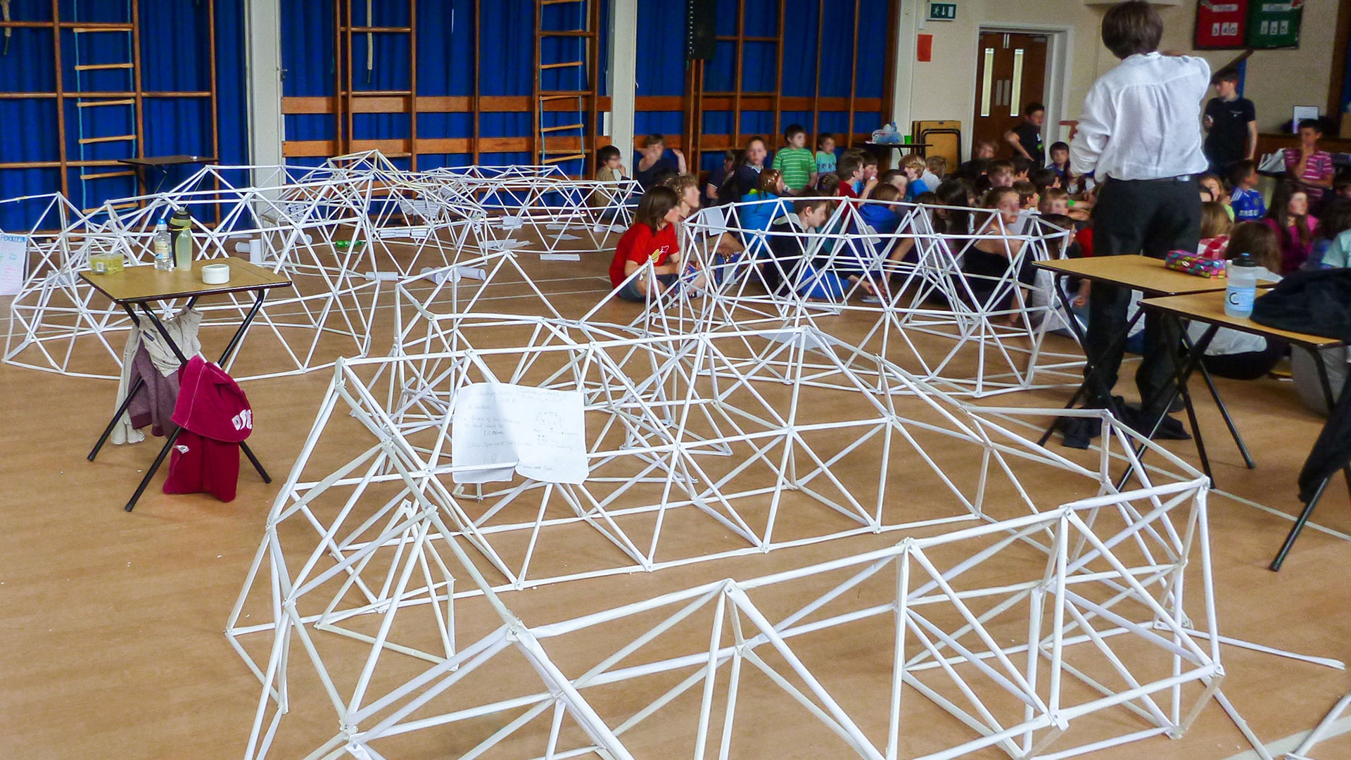 school hall with children learning different architectural designs made out of cardboard tubes