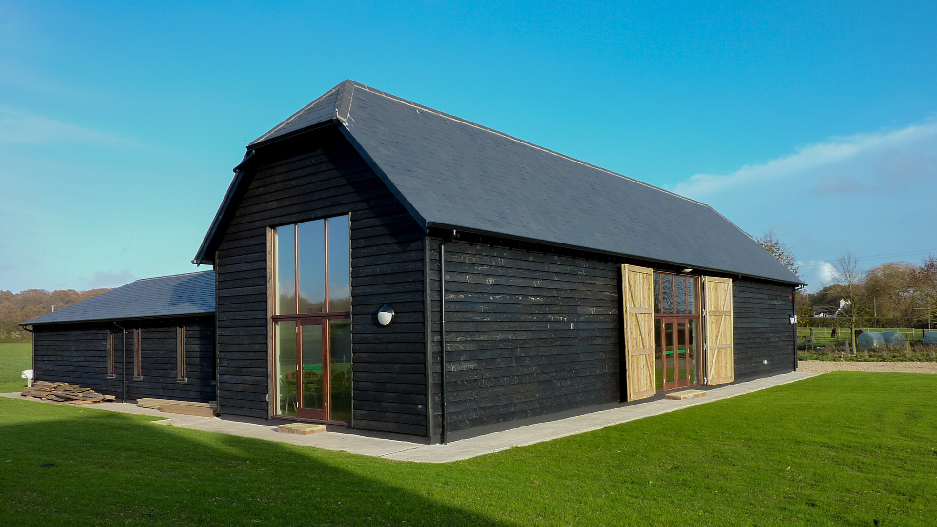 front view of large barn conversion with black wood cladding and double height windows