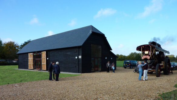large black barn with double height windows and a traction engine next to the building