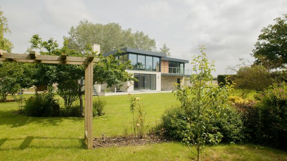 front view of beautiful modern house with stone and white wall and a flat roof taken from garden behind shrubbery