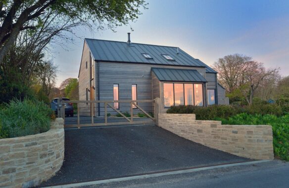 Modern rural house with timber cladding and metal roof view from road at dusk with lights on