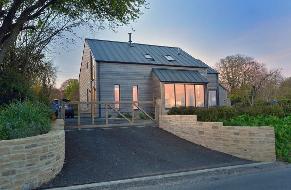 Modern rural house with timber cladding and metal roof view from road at dusk with lights on