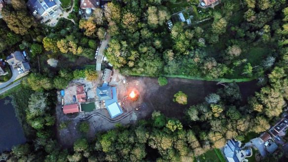 aerial view of large house surrounded by trees and fire pit burning next to house