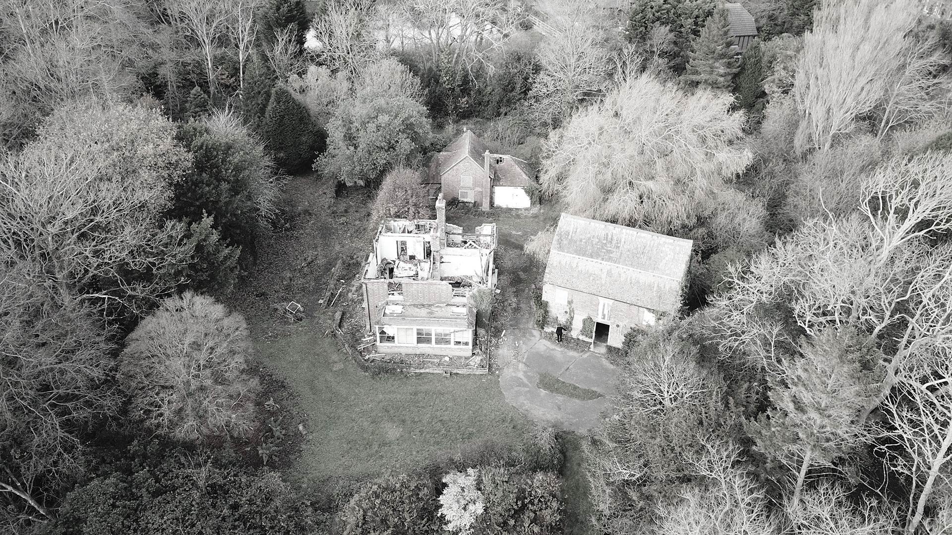 aerial view of existing house with roof collapsed, surrounded by trees