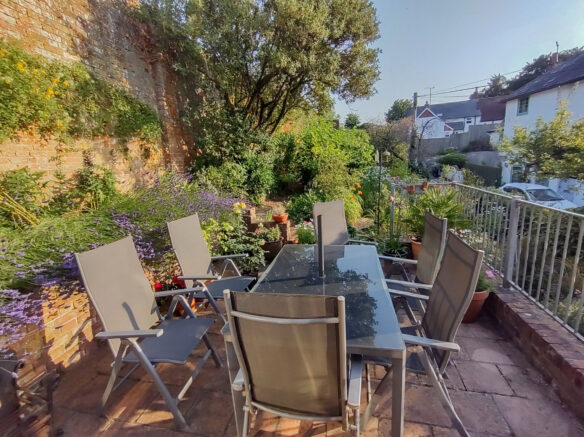 raised patio area with table and chairs surrounded by beautiful flowers and brick wall