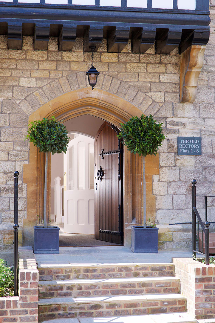 steps leading to beautiful entrance with large wooden door and stone walls below oriel window