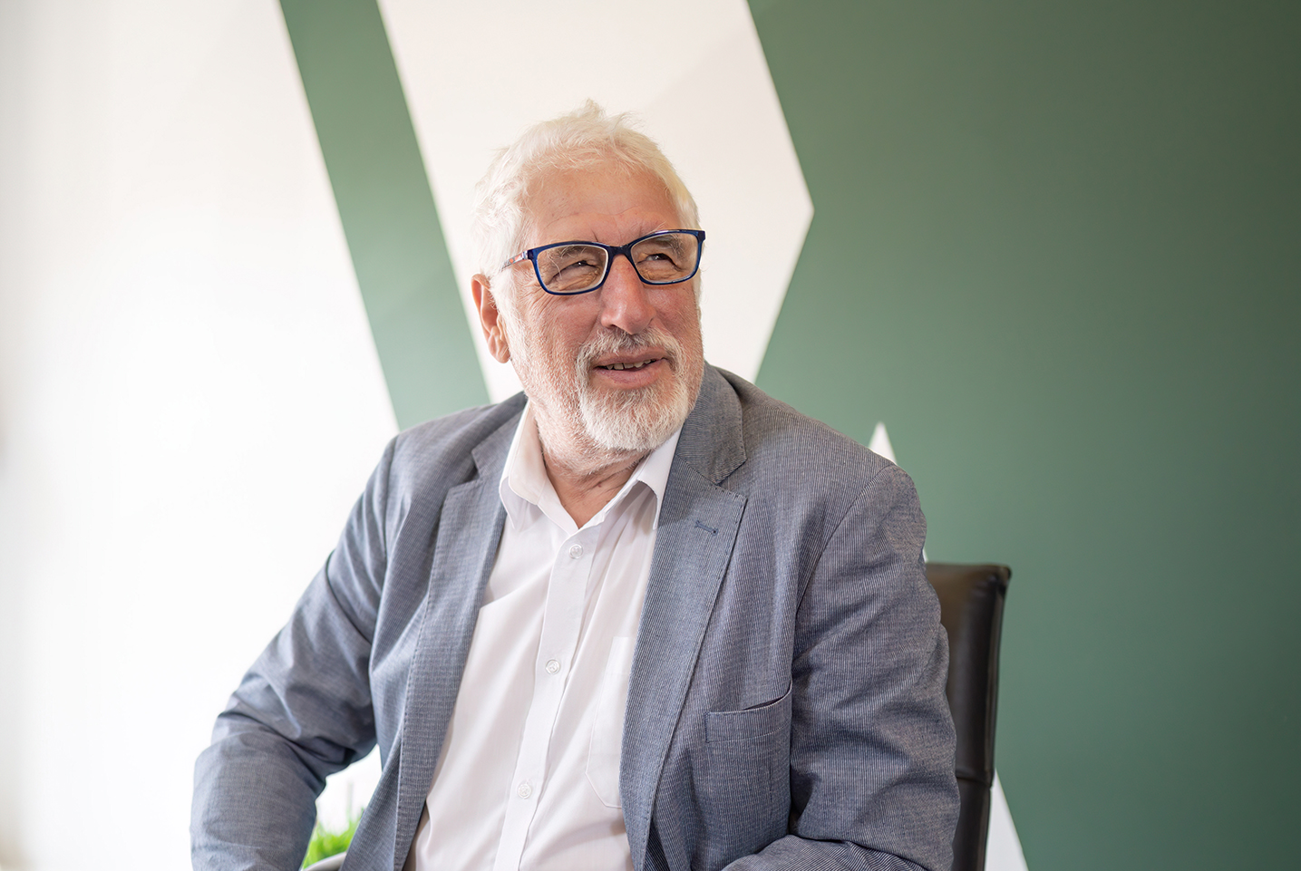 man smiling looking beyond the camera sat down with green and white background