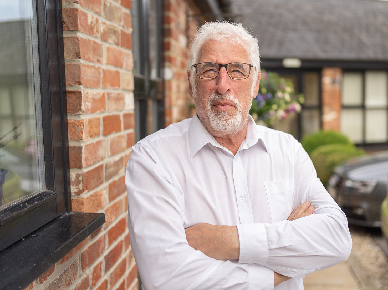 man in white shirt with crossed arms stood next to wall