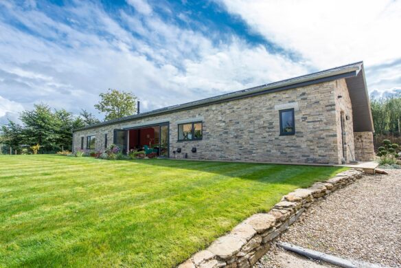 side view of single storey stone house with large glass sliding doors leading onto lawn garden