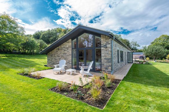 elevation end of stone walled house with decked patio and large grass lawn