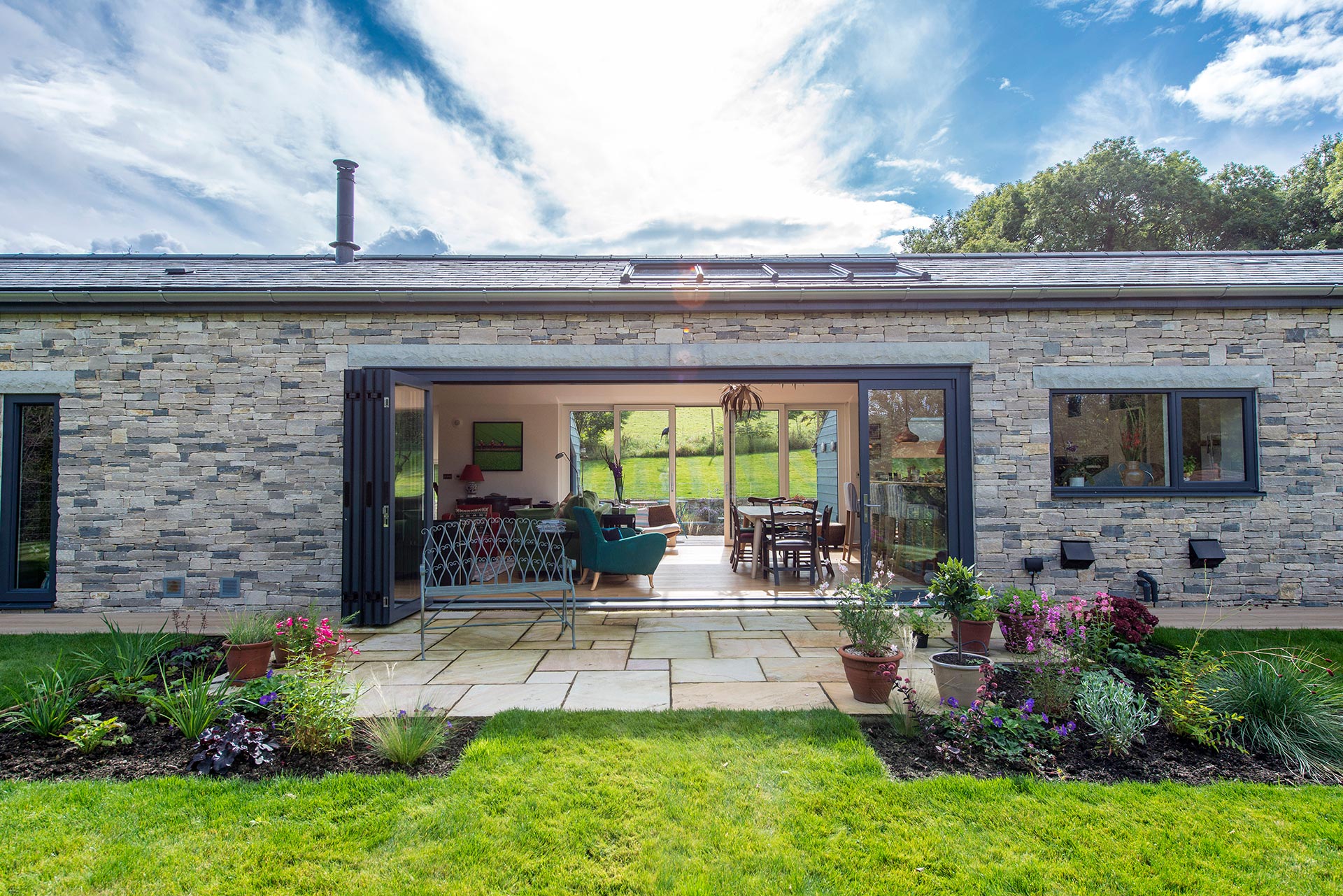 single storey stone house with large glass sliding doors leading onto patio and lawn garden