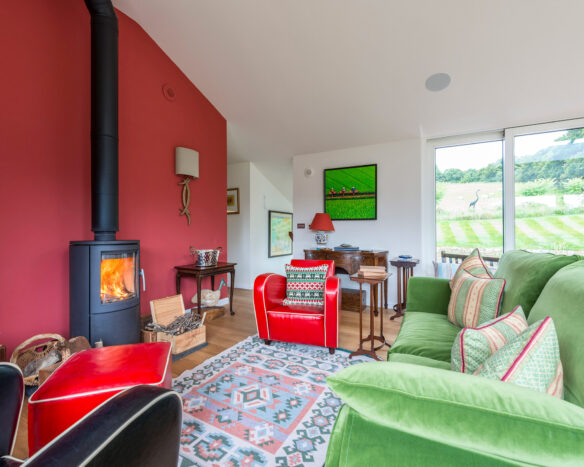 living room with red and green sofas, log burner lit and red featured wall