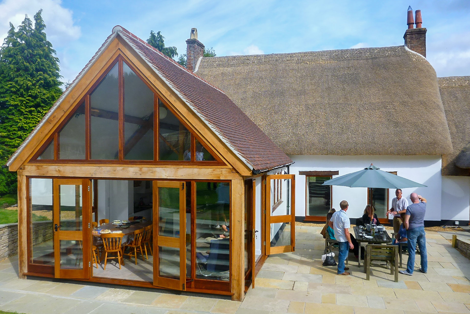 finished extension with red roof and wood frame attached to white traditional house with thatched roof