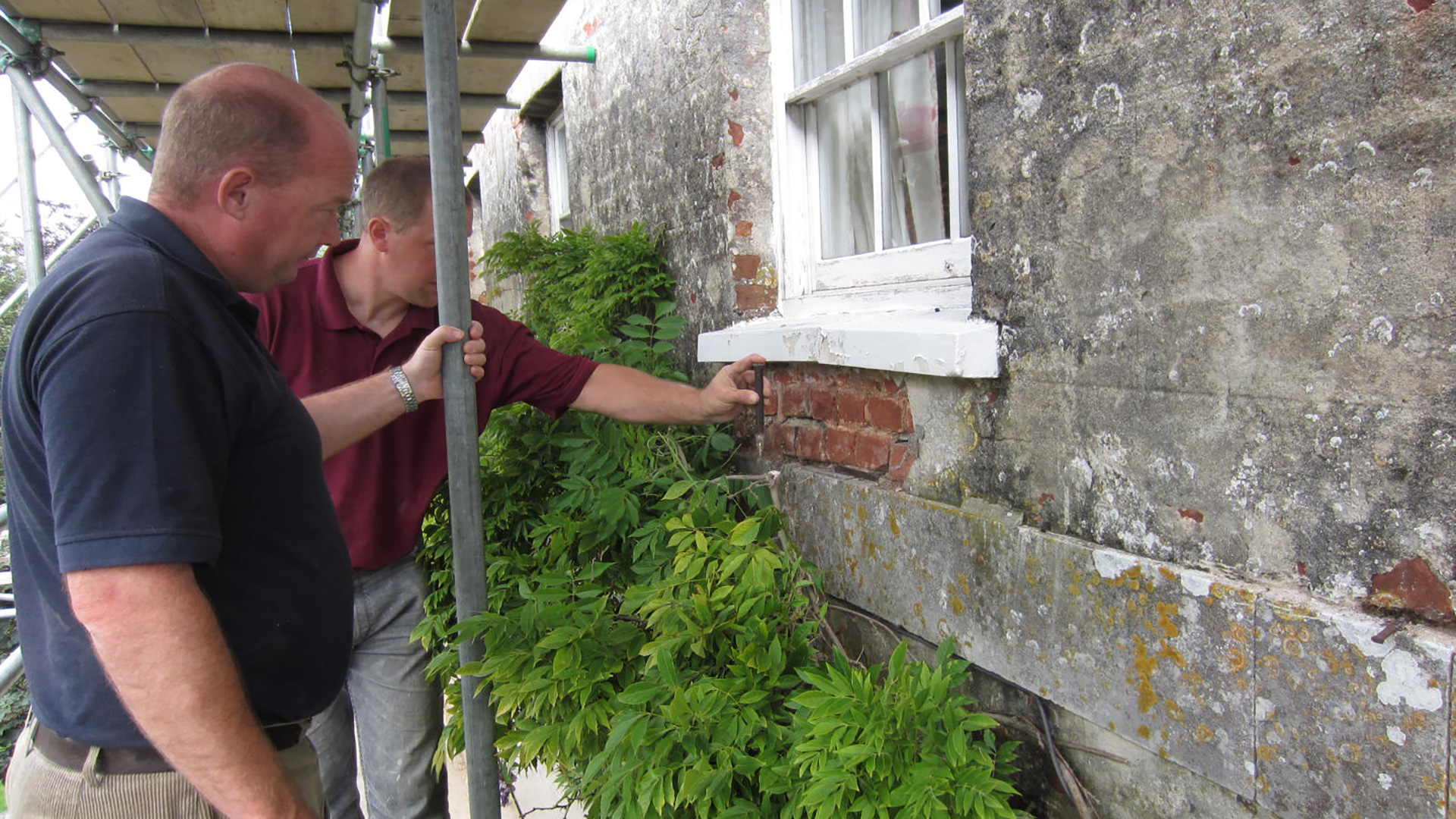 Two men looking at stonework under window