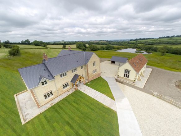 aerial view of stone farmhouse and annex with lake behind