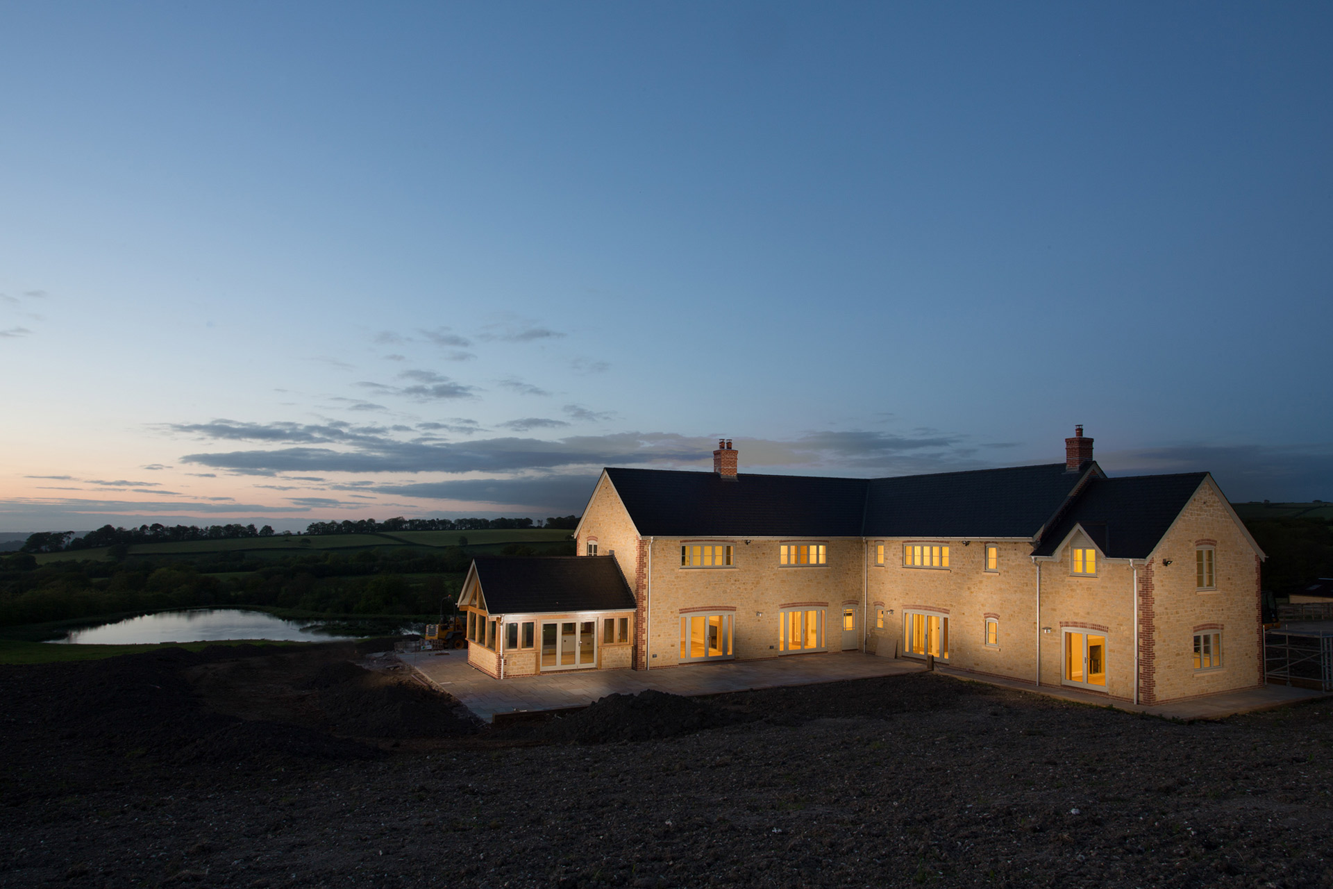 view of finished farm house at night with lights on and lake behind