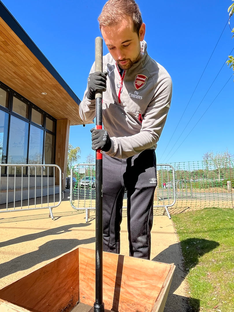 man compacting soil in bucket with pole