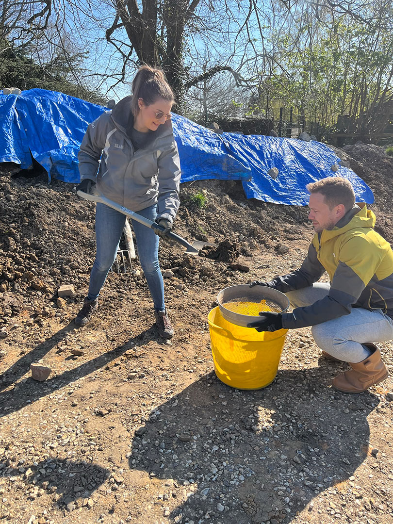 two people filtering soil into bucket