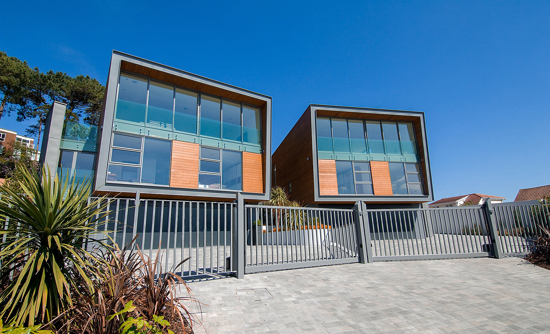 front view of two houses with timber cladding and zinc detail with gates in front of driveway