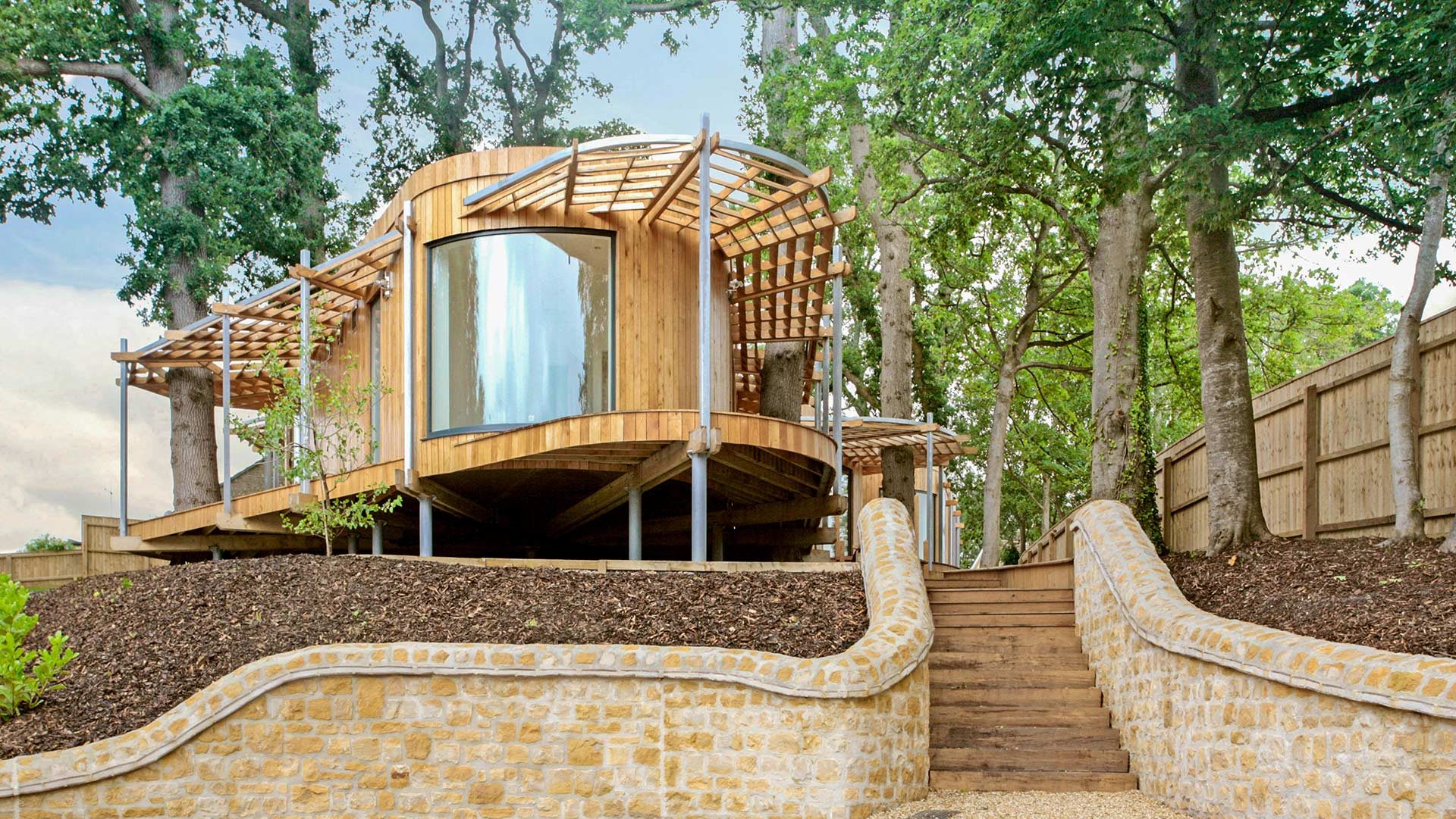 front view of timber cladded house in pod style surrounded by trees from driveway