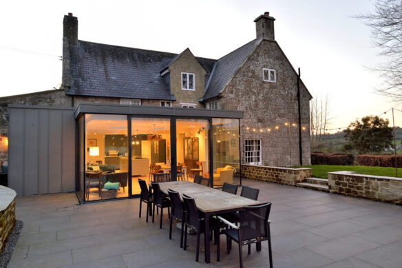modern extension of traditional stone house with large patio area taken at dusk with lights on