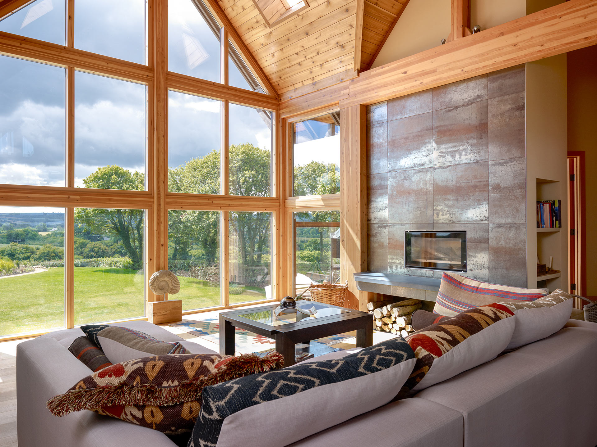 large living room space with inbuilt fire place in wall and large double height vaulted ceilings and feature window wall looking out to countryside