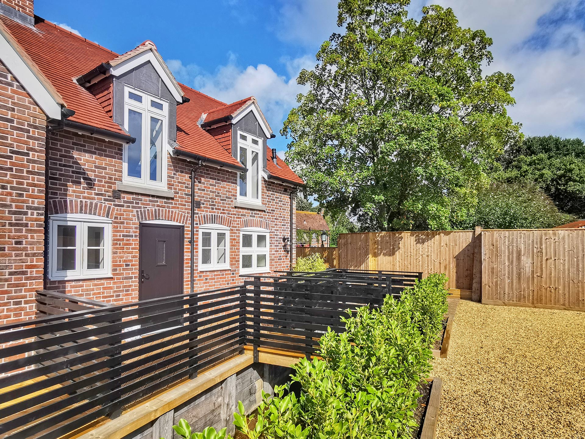 rear view of red brick house with walkway over river leading to graveled parking area