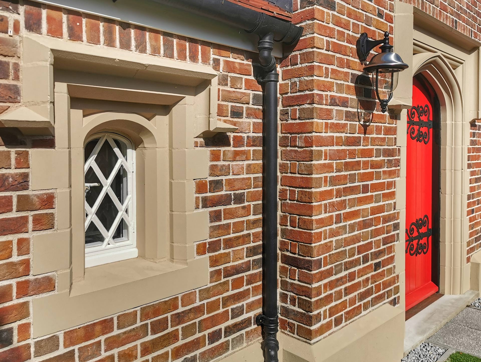 detail photo of red brick house with red feature door and small window with leaded lights