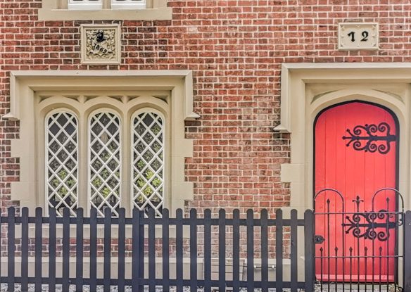 detail of house with red front door and feature windows behind black fence