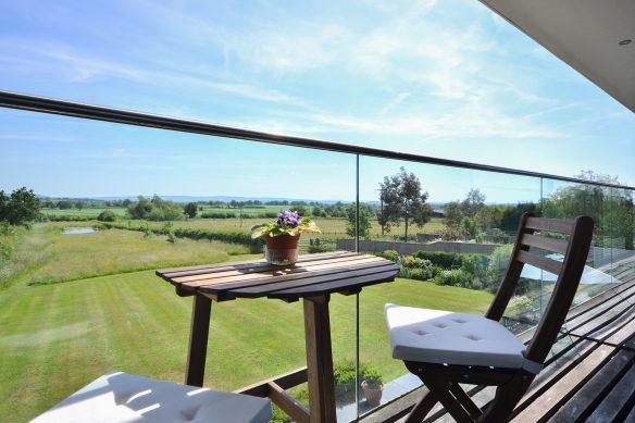 view of beautiful countryside from balcony with glass balustrade and table & chairs