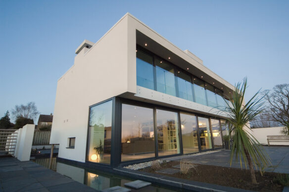 rear view of contemporary house with large glass windows and balcony taken at dusk with lights on