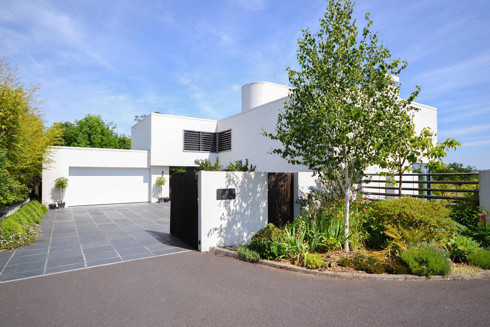 approach view to modern house with white wall and trees & plants in front