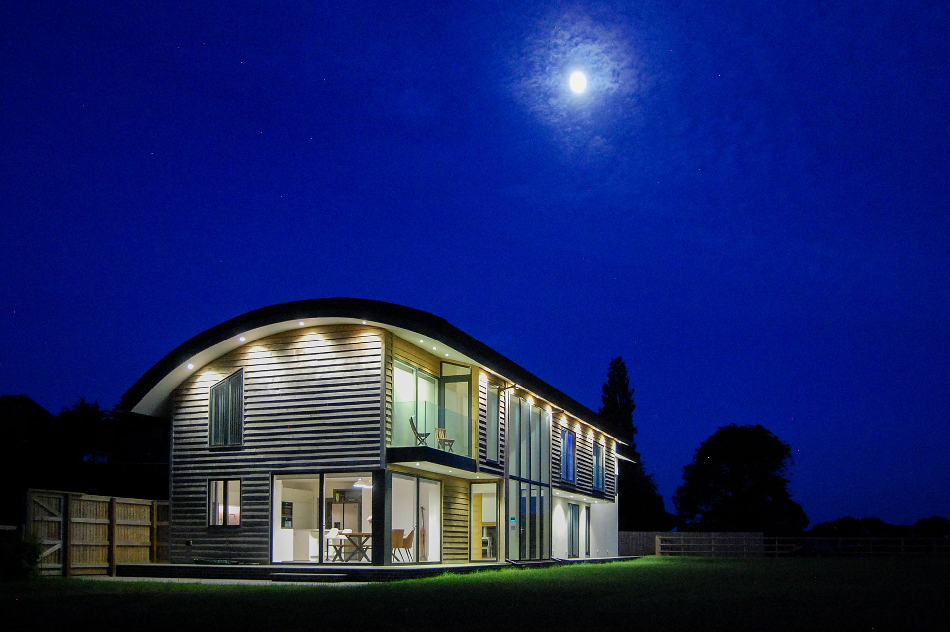 exterior garden view of house with curved sedum roof taken at night with lights on